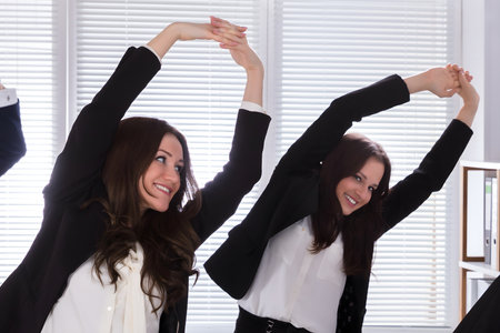 Happy Businesspeople Doing Stretching Exercise Behind Desk At Workplaceの写真素材