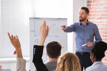 Businesspeople With Hands Raised Answering Businessman In Conference At Office