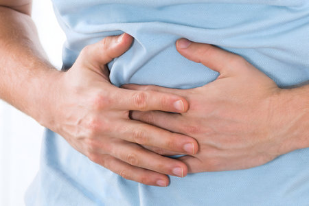 Close-up Of Young Man Suffering From Stomach Ache Standing At Homeの写真素材