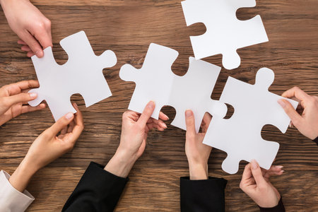 High Angle View Of Businesspeople Hand Solving Jigsaw Puzzleの写真素材