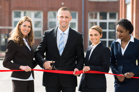 Happy Businesspeople At Opening Cutting Ribbon With Scissor