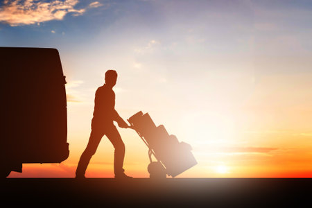 Silhouette Of Delivery Courier With Cardboard Boxes On Trolley Near The Van At Sunsetの写真素材