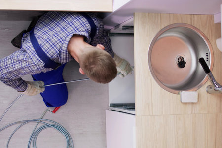 Plumber cleaning clogged drain pipe to unclog it