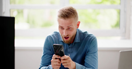 Amused Man Celebrating With Cellphone At Office