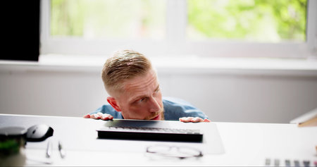 Scared Man Hiding Behind Office Desk In Room