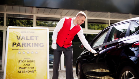 Personalized Luxury Valet Service: A Young Businessman Receives Receipt from Uniformed Attendant in Modern City Setting. Professionalism and Satisfaction Guaranteed.の写真素材