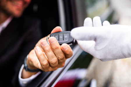 Experienced businessman passing car key to valet driver at hotel entrance, symbolizing trust and...