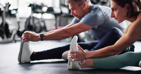 Leg Stretch Exercise In Gym. Couple Doing Sports