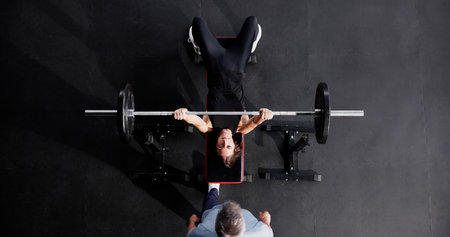 Woman Doing Bench Press In Fitness Club With Coach