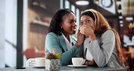 Black Businesswoman Sharing Gossip with Friend at Cafeの写真素材