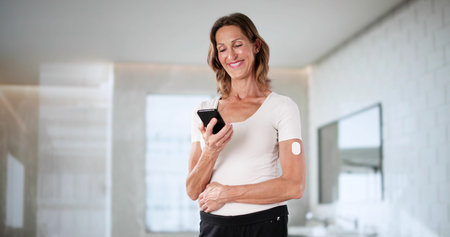 Diabetic Woman Checking Blood Sugar Levels On Smartphone In Bathroom