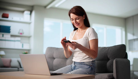 Young Woman Sits On Sofa, Smiling While Holding Mobile Phone.
