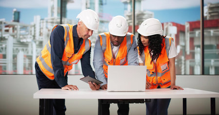 Diverse Group Of Industrial Engineers Using Laptops At Gas Production Facility.