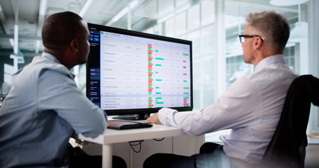 Focused Business Team Analyzing Reports On Multiple Computer Screens Together.