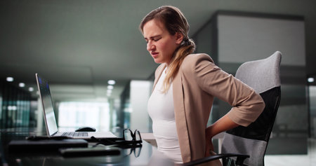 Woman With Poor Posture Sits In Chair, Dealing With Backache.の写真素材