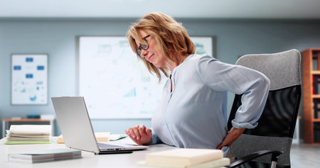 Woman In Office Struggles With Lower Back Pain From Poor Posture.の写真素材