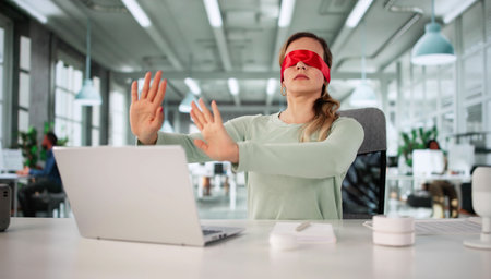 Confused Blindfolded Woman Struggling With Laptop In Corporate Office Setting.の写真素材