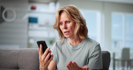 Distraught Elderly Woman Holds Broken Smartphone, Seeking Tech Support Helpの写真素材