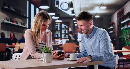 Happy Couple Sharing Smartphone App At Cafe Owned By Man.の写真素材