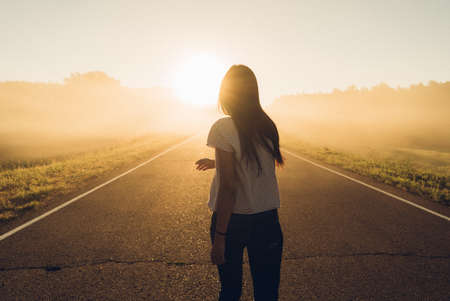 woman stand on the road with tree around, Asian traveler girl stand turn back on the road with sunshine and tree of parklandの写真素材