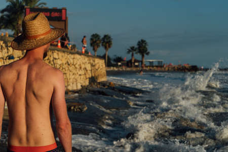 The guy in the hat standing on the beach and watching the waves at sunsetの写真素材