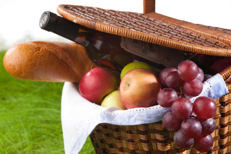 Picnic basket with wine, fruits and baguette on green grass, isolated on white backgroundの写真素材