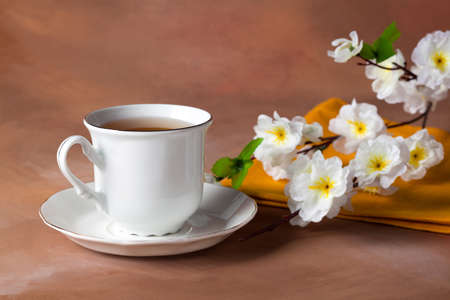 still life with cup of tea and cherry blossom on brown background