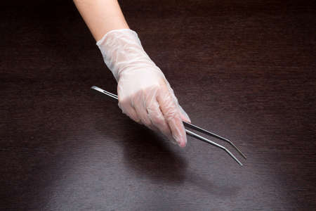 hand in medical glove with tweezers on wooden table
