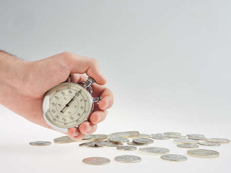 time is money. hand holding a stopwatch on a background of silver coinsの写真素材
