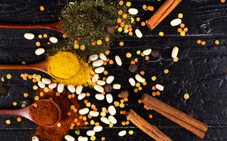 wooden spoons with multicoloured seasonings on a black textured table. background for kitchenの写真素材