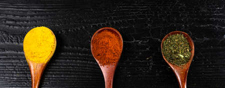 wooden spoons with multicoloured seasonings on a black textured table. background for kitchenの写真素材
