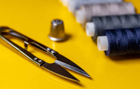 Sewing accessories. Colored spools of thread, scissors on a yellow background