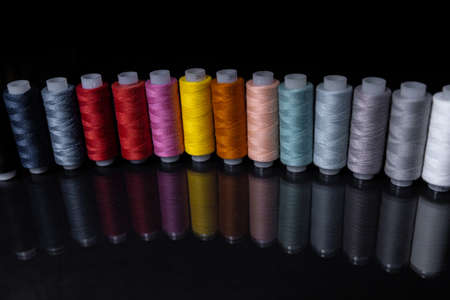Spools with multi-colored threads stand in a row on a mirror surface.の写真素材