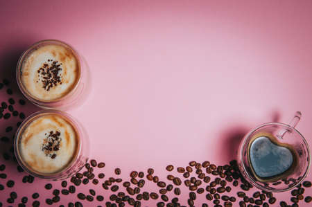 Two cups of cappuccino and a mug in the form of a heart with coffee on a pink background among coffee beans. Frame for text. Copy space.の写真素材