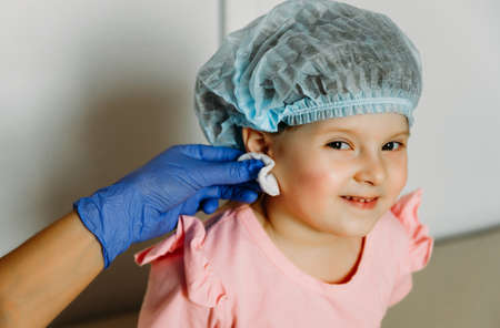 Little beautiful girl smiles and looks into the camera. Waiting for the doctor to clean the ear and...