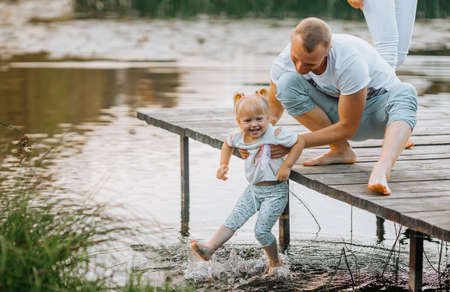 A man with a kid on a wooden bridge of a pier near the lake surrounded by water lilies and grass summer time. Father and child together in the countryside outdoors. Family on the background of nature.の写真素材