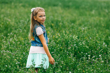 Beautiful girl with blue eyes in a field among flowers and green grass.の写真素材