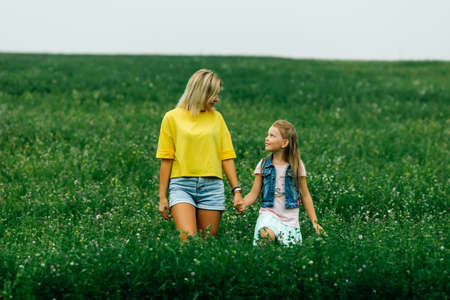 Sunny portrait of mother and daughter together with wild multicolored flowers on a summer warm day, mom with baby outdoors.の写真素材