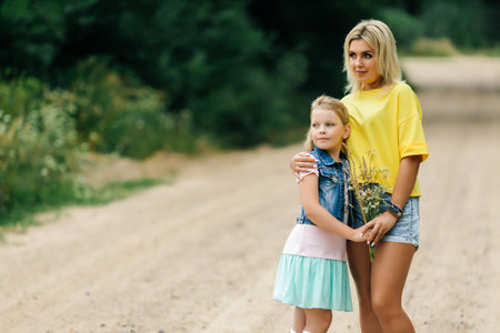 A young mother with her daughter, stand on the road in the forest and hug each other. Look away.の写真素材