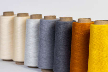 Close-up shot of bright colored bobbins with threads standing in a row one after another on white...