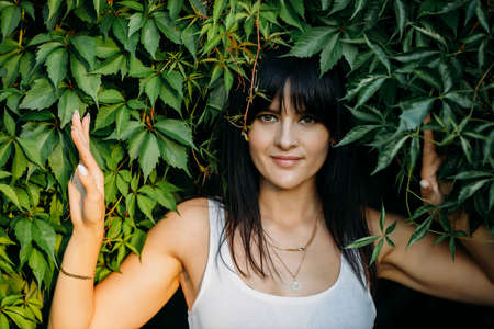 Portrait of a young beautiful brunette in ivy, summer park outdoors.