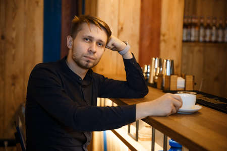 Close-up portrait of a young man sitting at a bar counter in a cafe with his head resting on his...