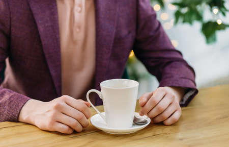 Close-up of male hands and a white cup with a plate. Lunch break. Tasty coffee.