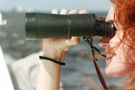 Beautiful red-haired girl looking through binoculars.の写真素材