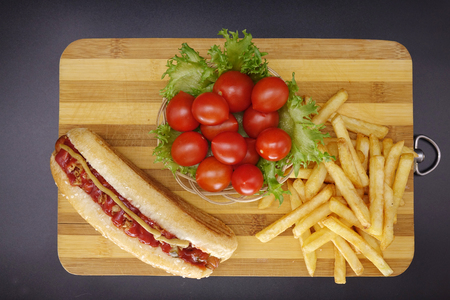 Hot dogs and French fries on black background. Sausages with tomato sauce and cherry tomatoes on a wooden Board.の写真素材