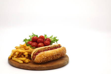 Hot dogs and French fries on white background. Sausages with tomato sauce and cherry tomatoes on a wooden Board.の写真素材