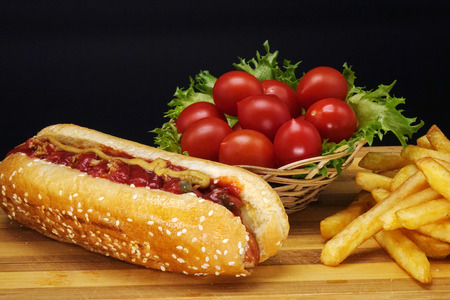 Hot dogs and French fries on black background. Sausages with tomato sauce and cherry tomatoes on a wooden Board.の写真素材
