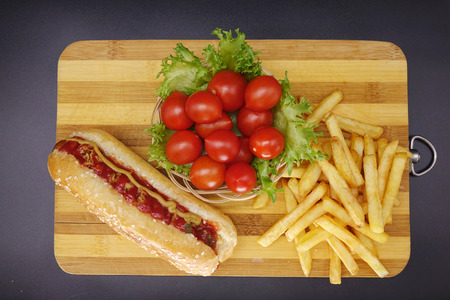 Hot dogs and French fries on black background. Sausages with tomato sauce and cherry tomatoes on a wooden Board.の写真素材