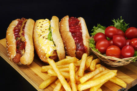 Hot dogs and French fries on black background. Sausages with tomato sauce and cherry tomatoes on a wooden Board.の写真素材