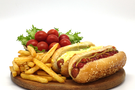 Hot dogs and French fries on white background. Sausages with tomato sauce and cherry tomatoes on a wooden Board.の写真素材